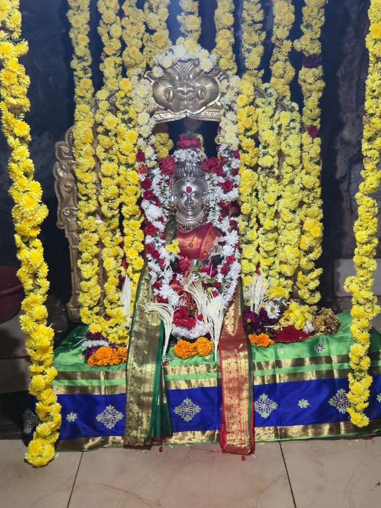 Deity decorated with garlands beneath a silver arch