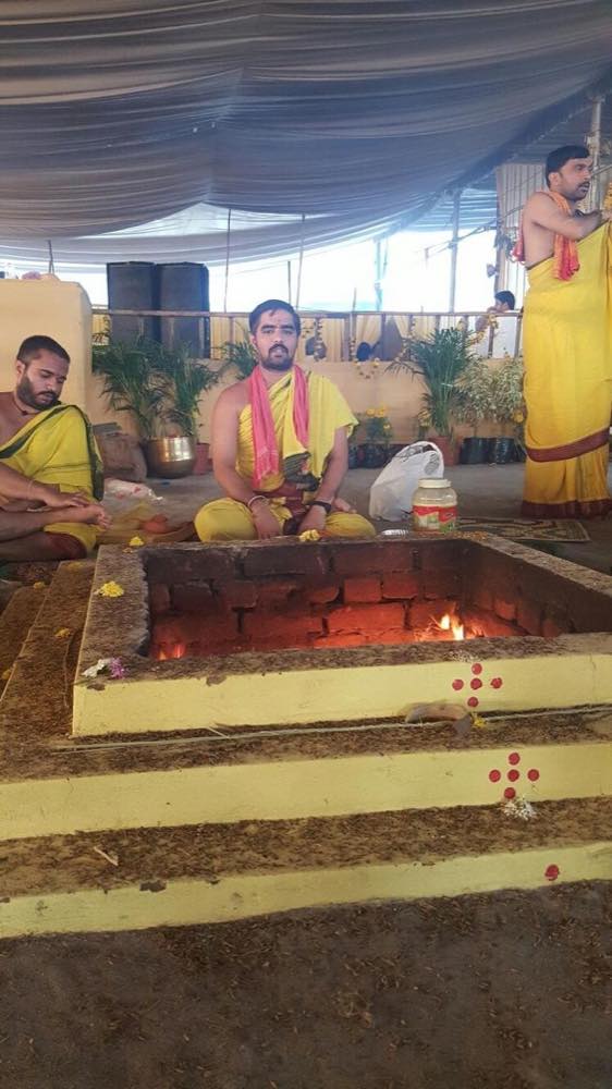 Fire burning in a square homa kunda, priests seated alongside