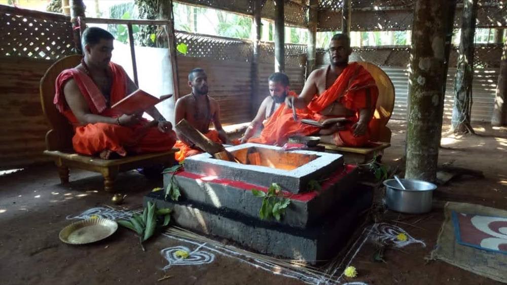 Four priests seated around a homa fire in an open mandapa