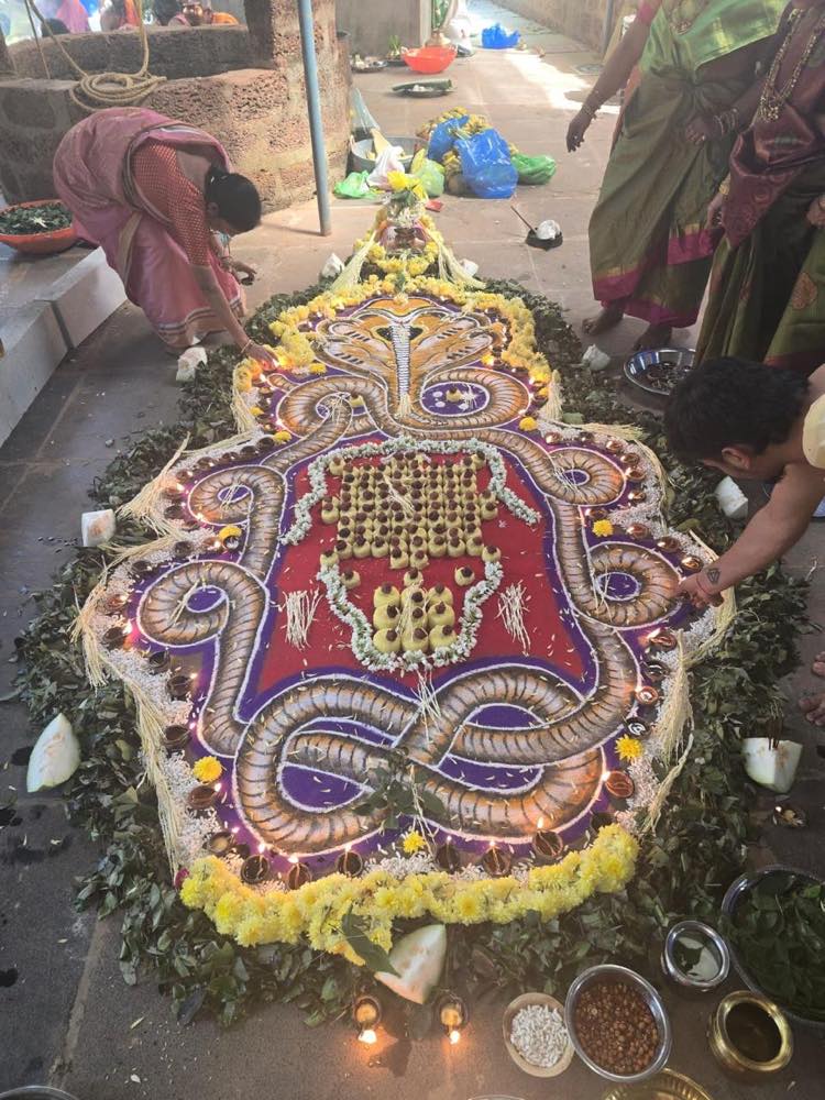Large serpent design drawn in coloured powder, ringed with oil lamps and offerings